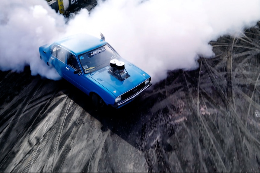 A blue car with smoke pouring out the back. 