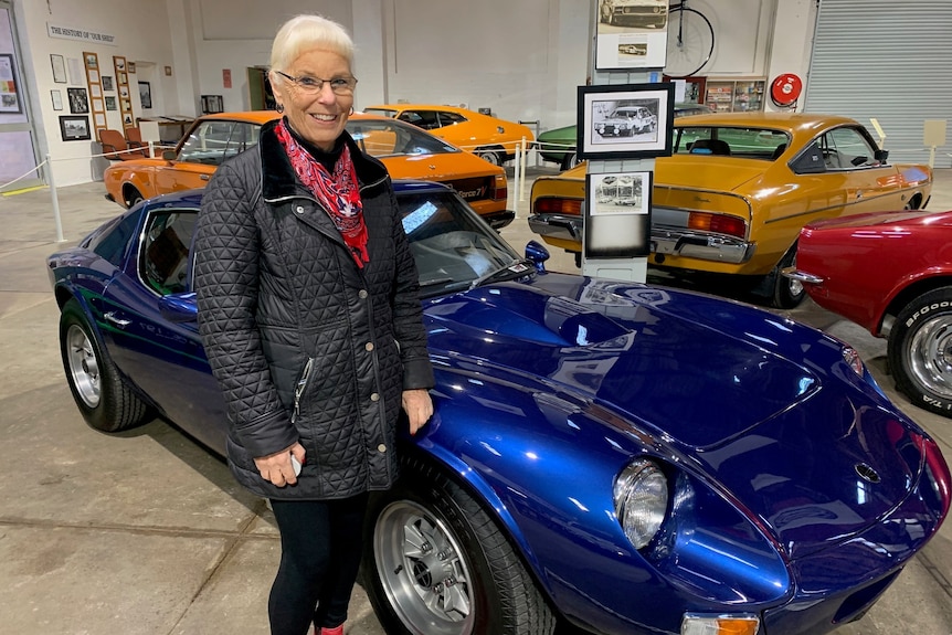 woman stands in front of midnight blue coupe 