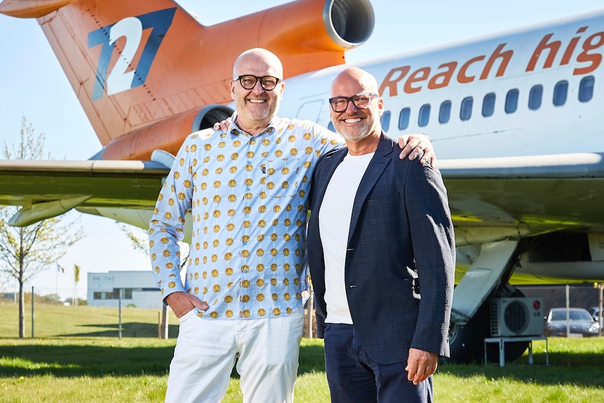 Two well-dressed men standing on grass with airplane tail behind.