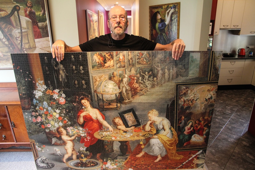 Gus Werthman stands in his home holding a 6000 piece puzzle