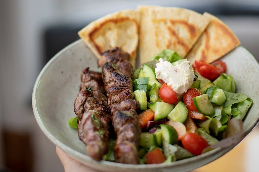 Red meat kebabs on a plate with a chunky salad and pieces of flatbread.