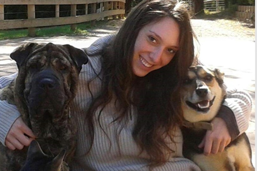 Dana hugs two dogs while sitting in a sunny yard