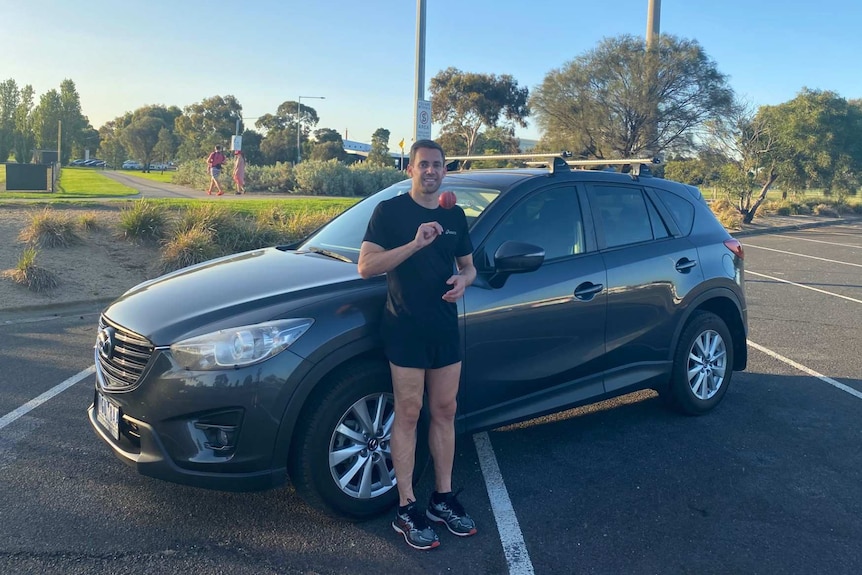 A man tosses a cricket ball in front of his car.