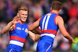 A Western Bulldogs AFL player smiles as he runs towards a teammate to congratulate him on kicking a goal.