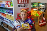 A woman with quaffed blonde hair with several grocery items named with puns on plastic.