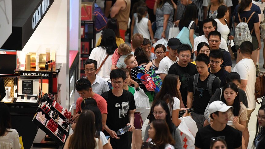 A packed shopping centre floor, filled with people walking and holding onto shopping bags.