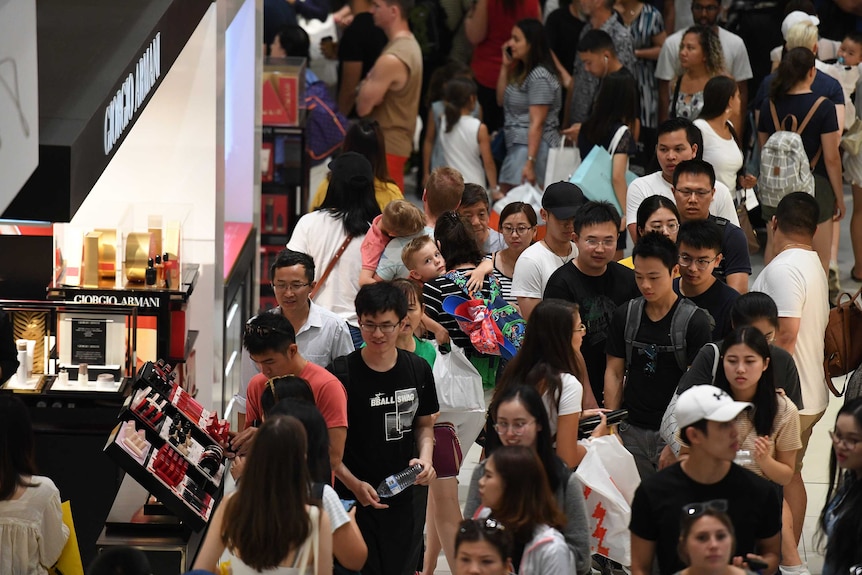 A packed shopping centre floor, filled with people walking and holding onto shopping bags.