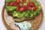 A brown plate is seen on top of a pink tabletop. There are two slices of sourdough on it, with smashed avocado and strawberries.