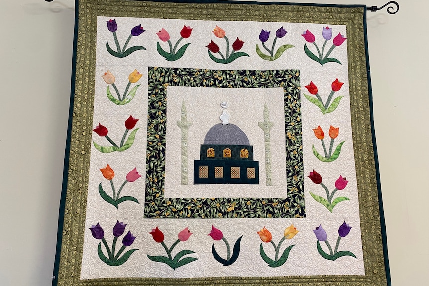 A tapestry of a mosque in the middle with tulips of different colours surrounding it.