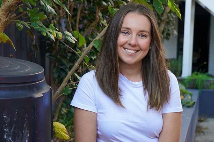 A young woman sits next to a compost bin