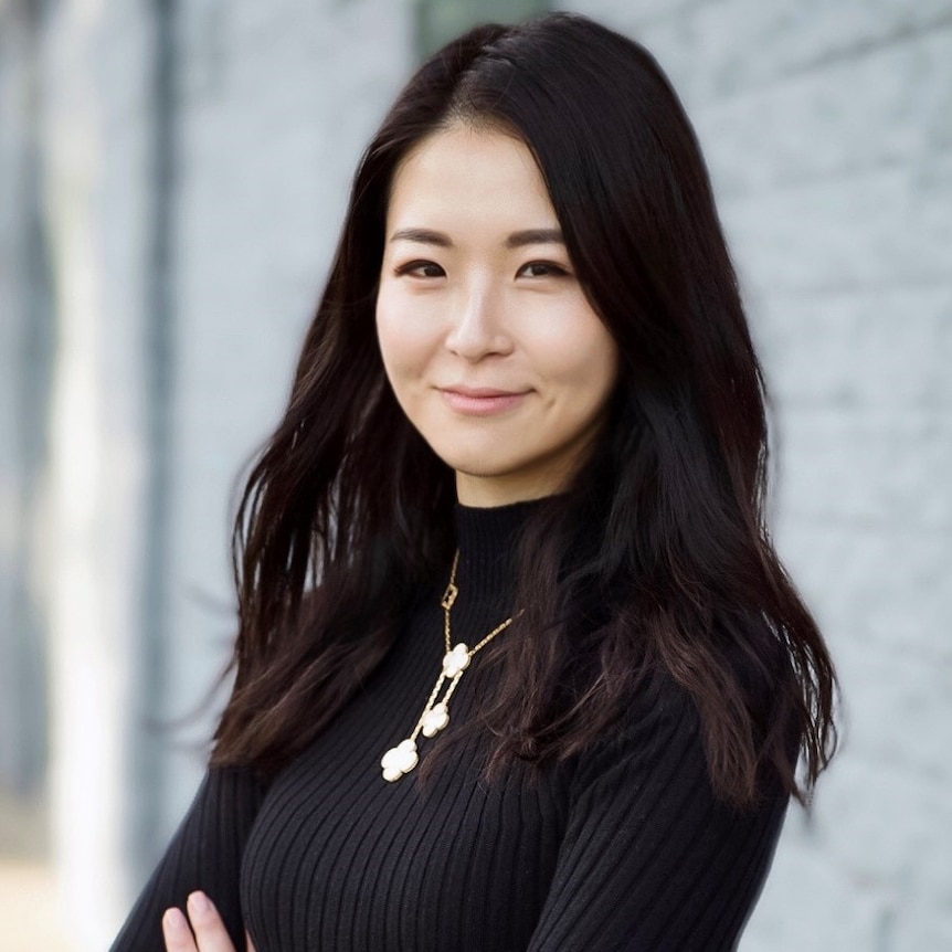 A young Chinese woman stands with her arms crossed looking at the camera.