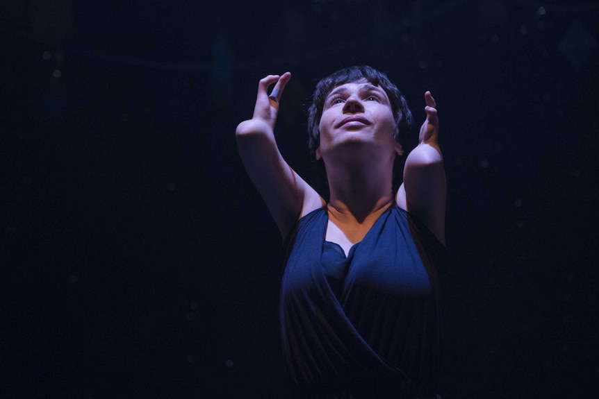 A woman with deformed arms wearing a dress in front of a dark background