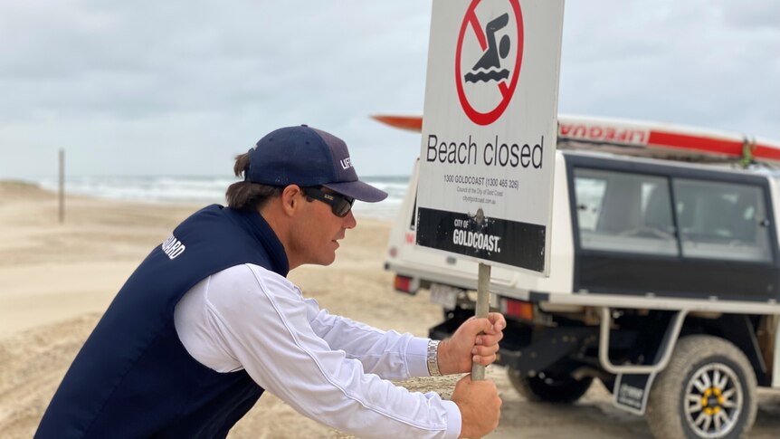 Lifeguard pushing 'beach closed' sign into sand.