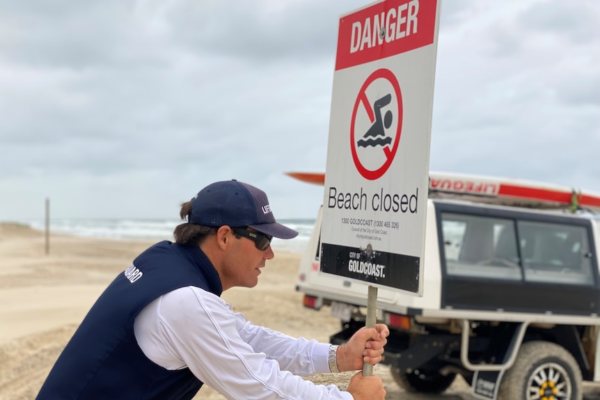 Lifeguard pushing 'beach closed' sign into sand.