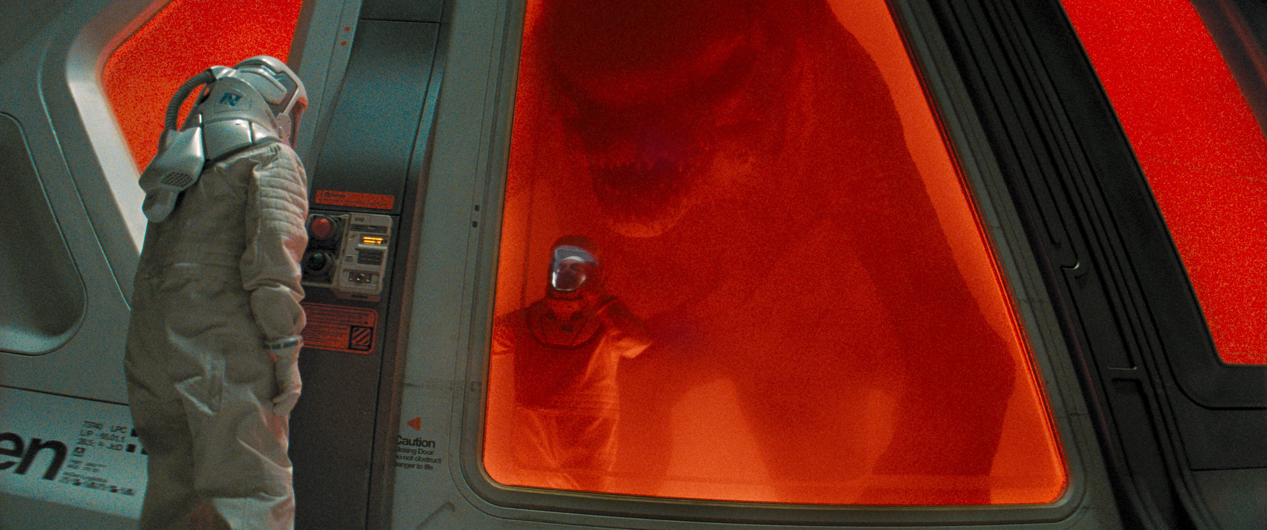 An inside view of a mutated Tyrannosaurus rex, or D.rex,walking ominously towards a person trapped on the outside.