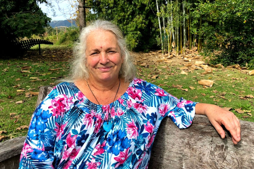 A woman wears a colourful dress and sits on a park bench