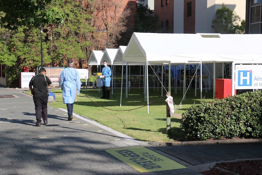 Three men, two of them wearing gowns and PPE, stand outside the RPH COVID clinic.