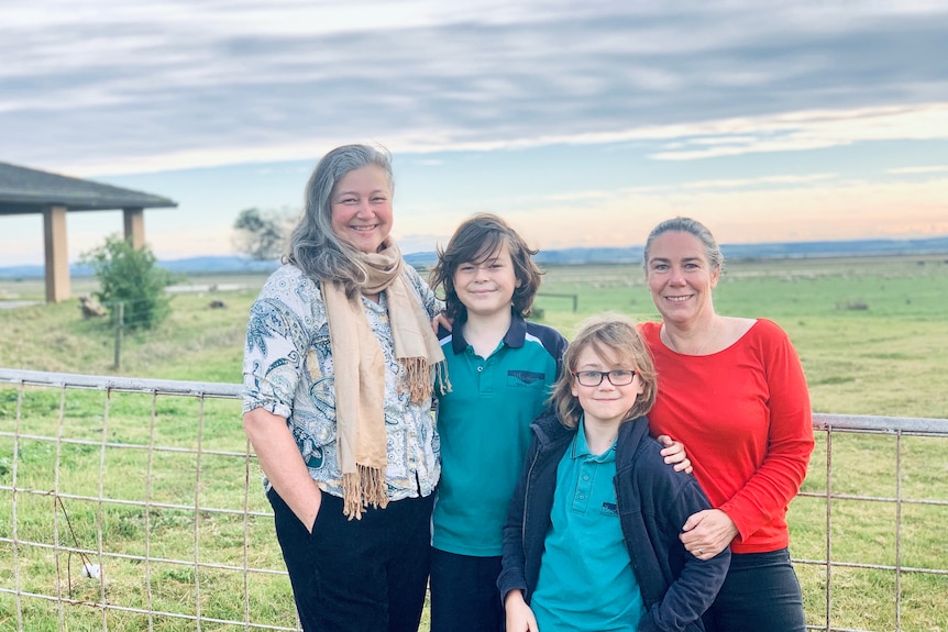 A family of four stand in front of a farm gate.