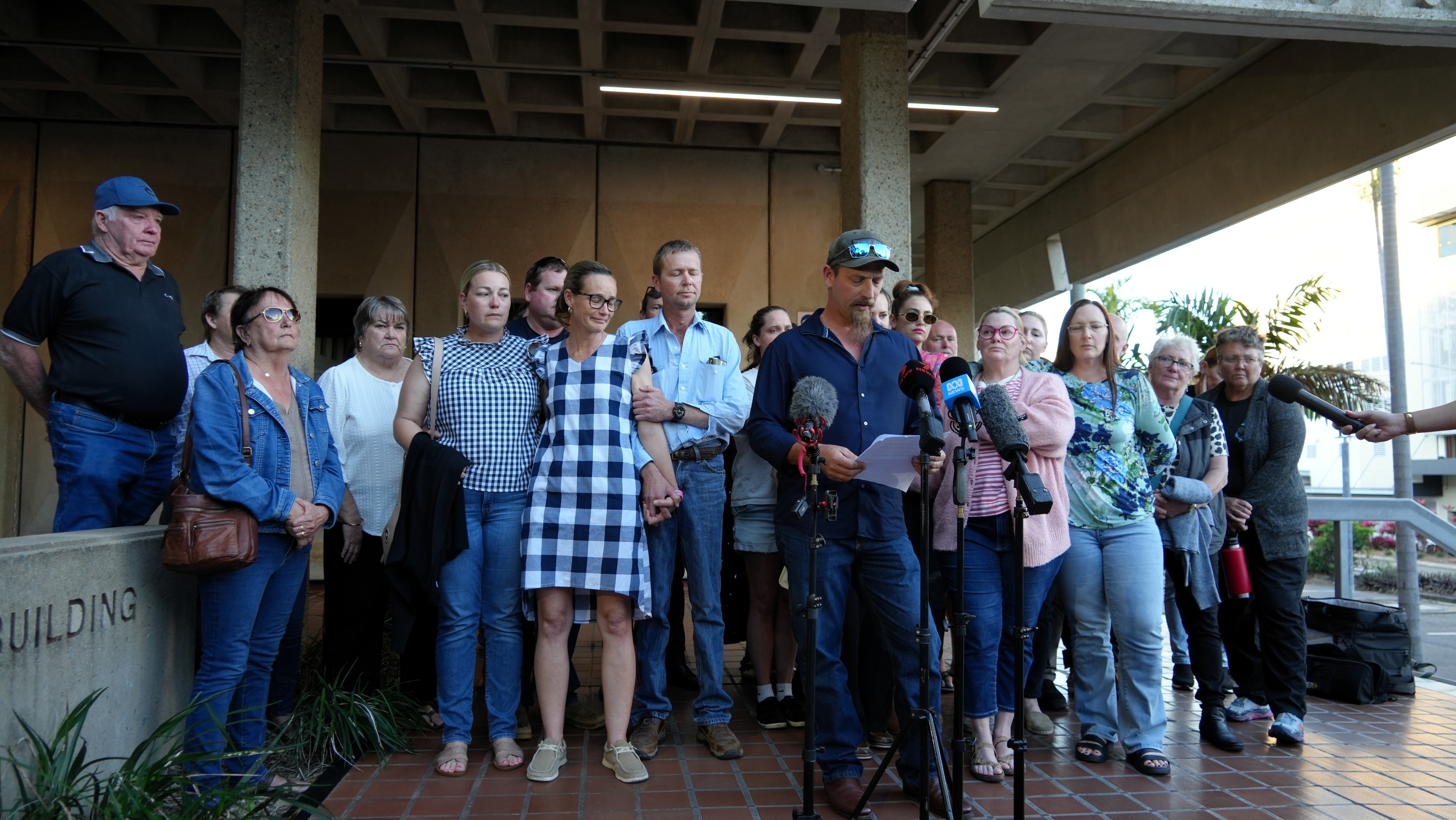 A large group of people outside of a court house standing around a microphone.