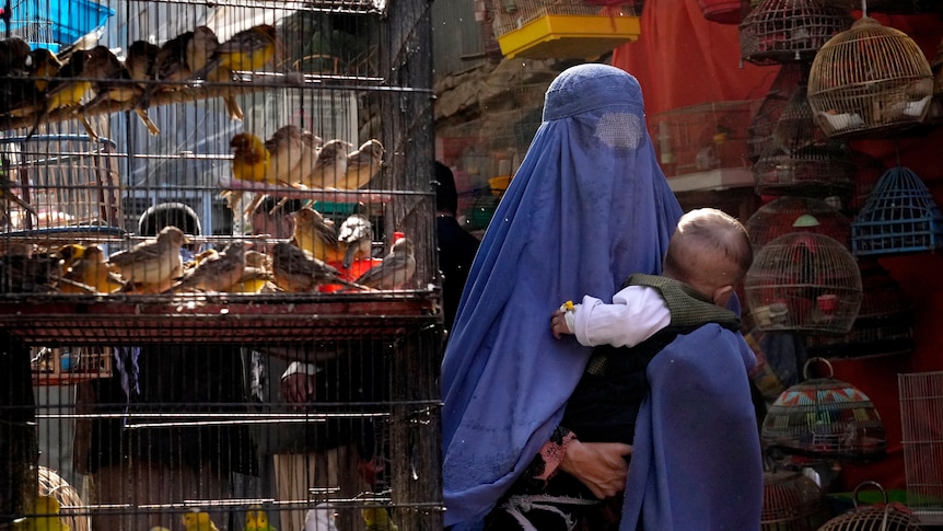 Woman wearing a burka, holding a child, walks through a bird market