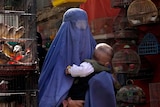 Woman wearing a burka, holding a child, walks through a bird market