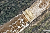 A birds eye view of water rushing over a catchment surrounded by trees.