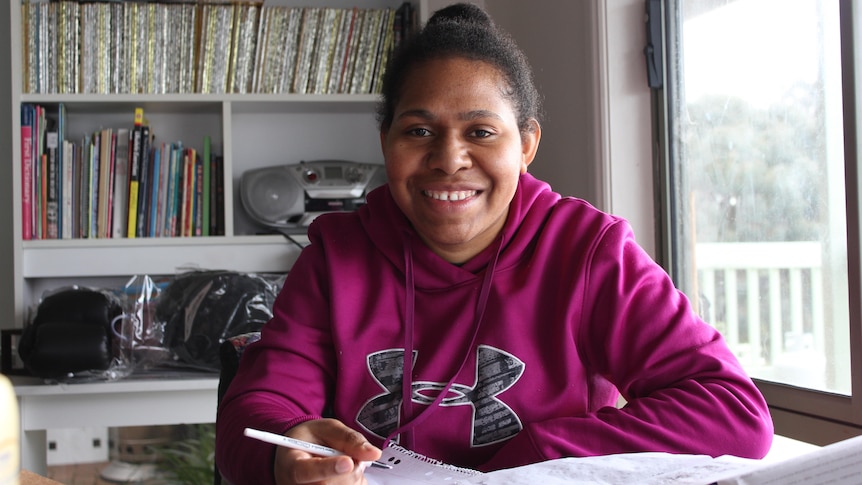 Sonia Paua smiles while sitting at a desk with a notebook and pen. 