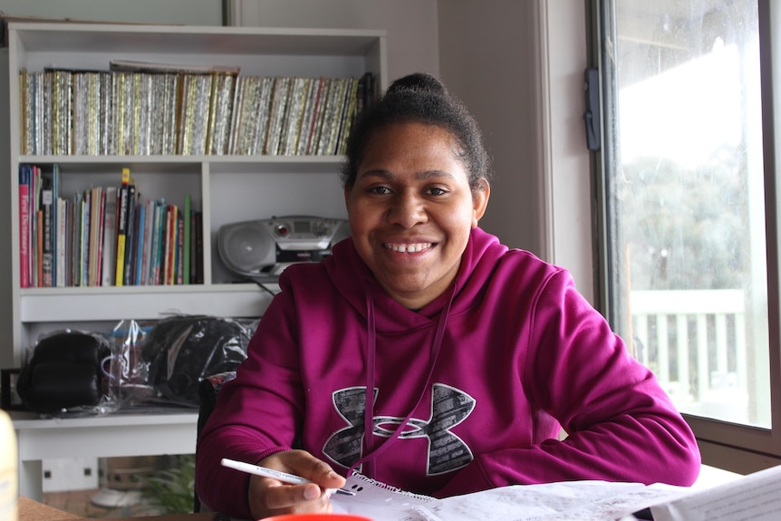 Sonia Paua smiles while sitting at a desk with a notebook and pen. 