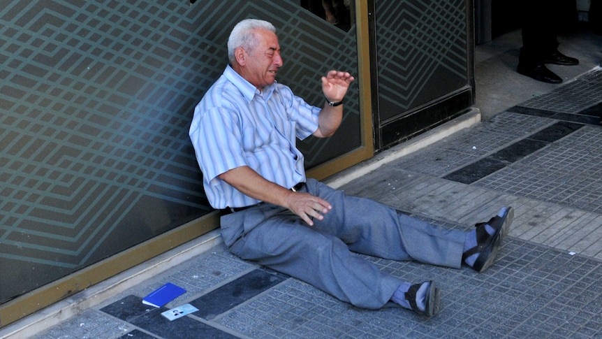 A pensioner sits on the ground outside a Greek national bank branch.