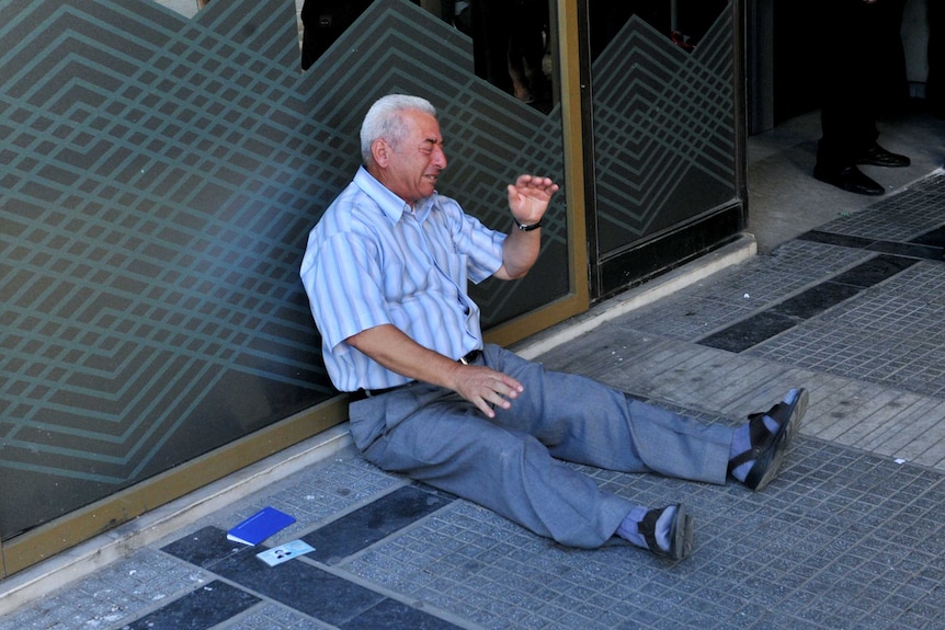 A pensioner sits on the ground outside a Greek national bank branch.