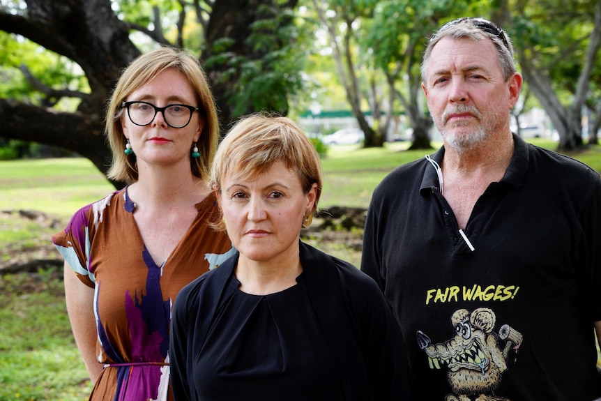 Kirsty Howey, Deborah Di Natale and Lloyd Pumpa are standing outside in a park with serious expressions. They look stern.