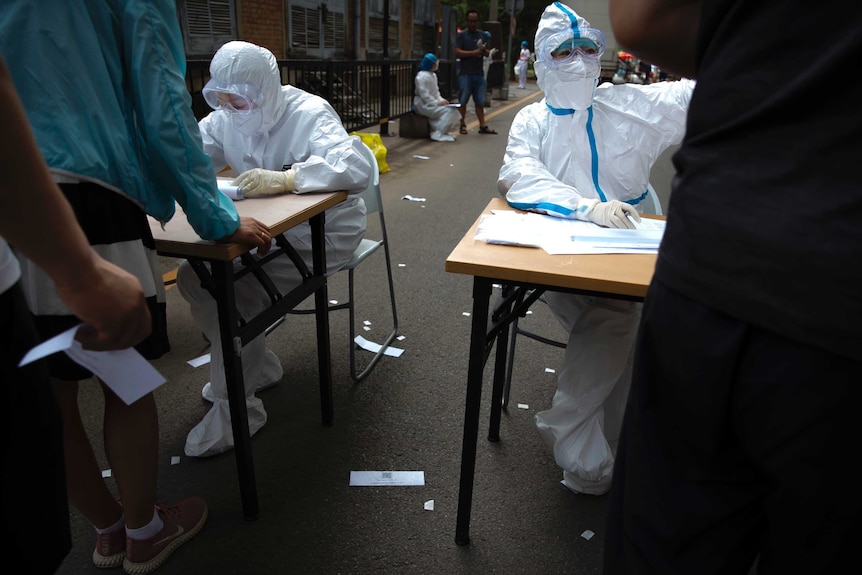 Workers in protective suits register people at a COVID-19 testing site for people potentially exposed to the Beijing outbreak.