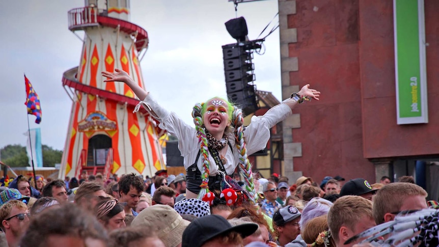 A woman sitting on a mans shoulder in the large crowd has her hands up