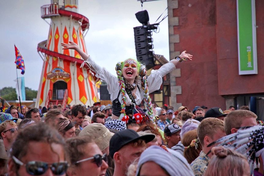 A woman sitting on a mans shoulder in the large crowd has her hands up