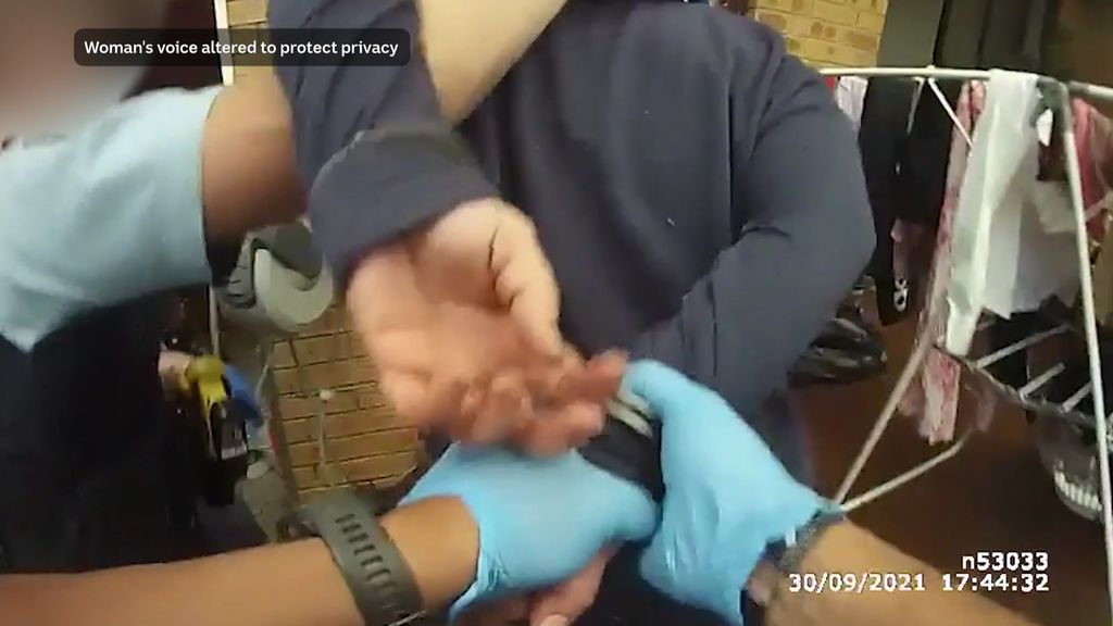 Police bodycam video frame shows woman being handcuffed by two officers in her yard.