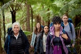 A group of five women hiking together with backpacks and warm clothes on in the Australian bush.