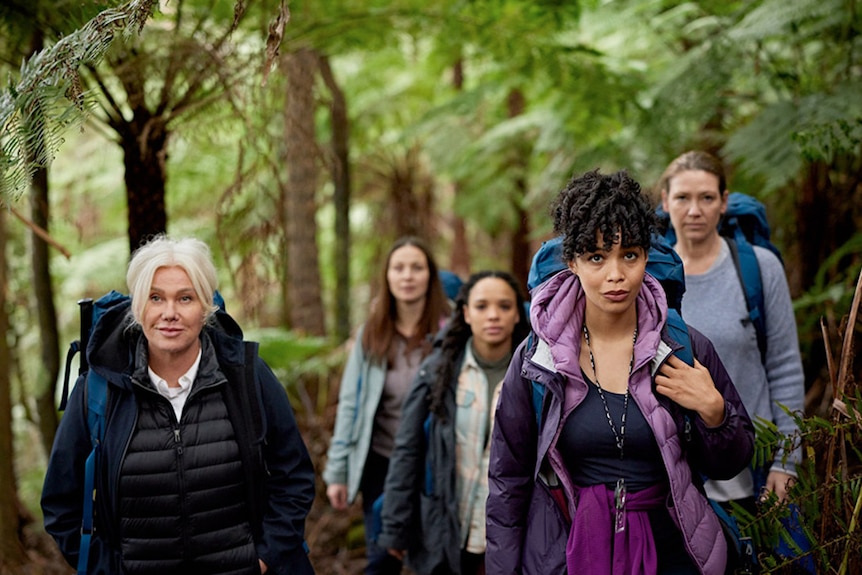 A group of five women hiking together with backpacks and warm clothes on in the Australian bush.