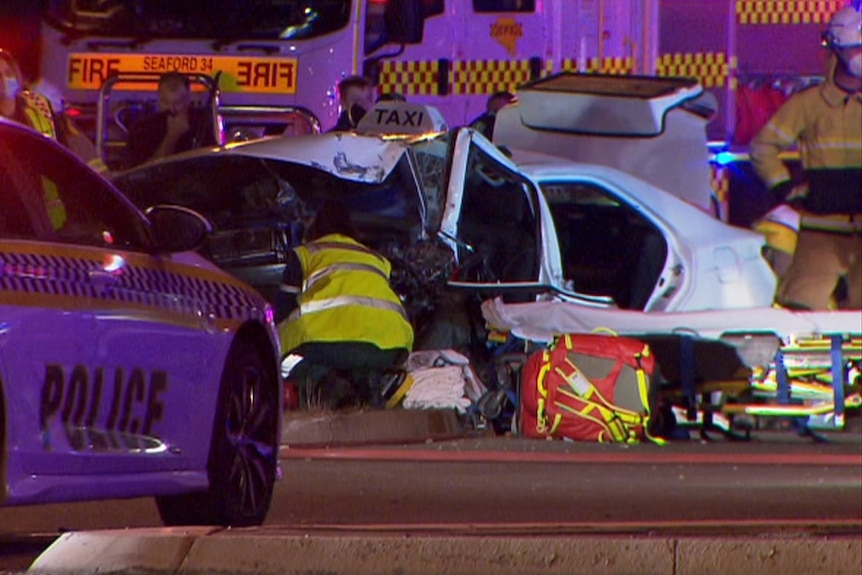 A police car and emergency workers at a damaged white taxi