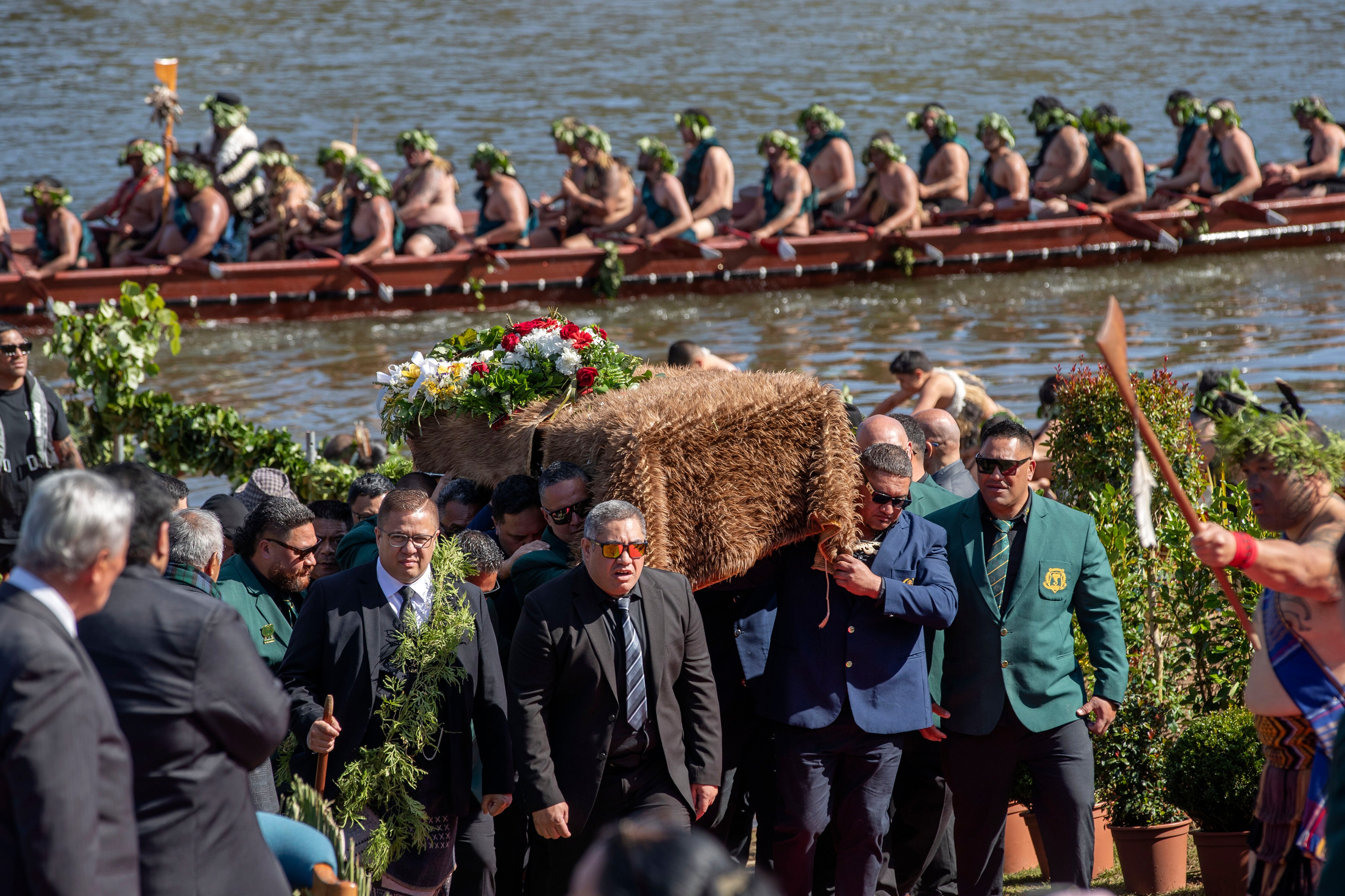 Pall bearers carry the coffin of New Zealand's Maori King, with a traditional canoe sitting on a river behind.