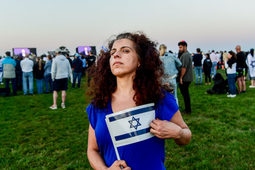 Tzipi Cohen Hyams with Israeli flags at public vigil in Sydney, crowd gathered behind her