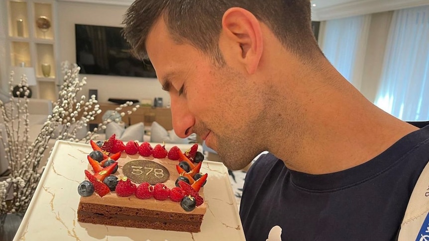 Novak Djokovic looks lovingly at a cake with 378 on it, celebrating the number of weeks he has spent as world number one.