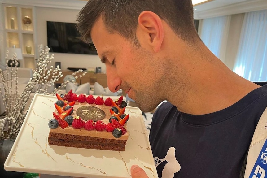 Novak Djokovic looks lovingly at a cake with 378 on it, celebrating the number of weeks he has spent as world number one.