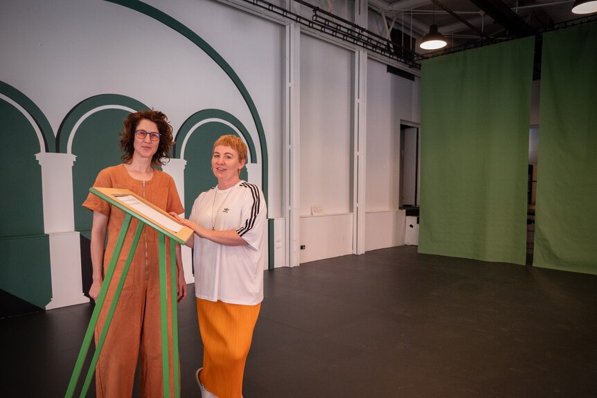 Two women stand in a new foyer room, with green arches painted on white walls.
