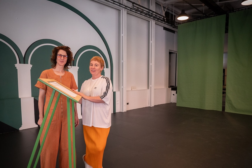 Two women stand in a new foyer room, with green arches painted on white walls.