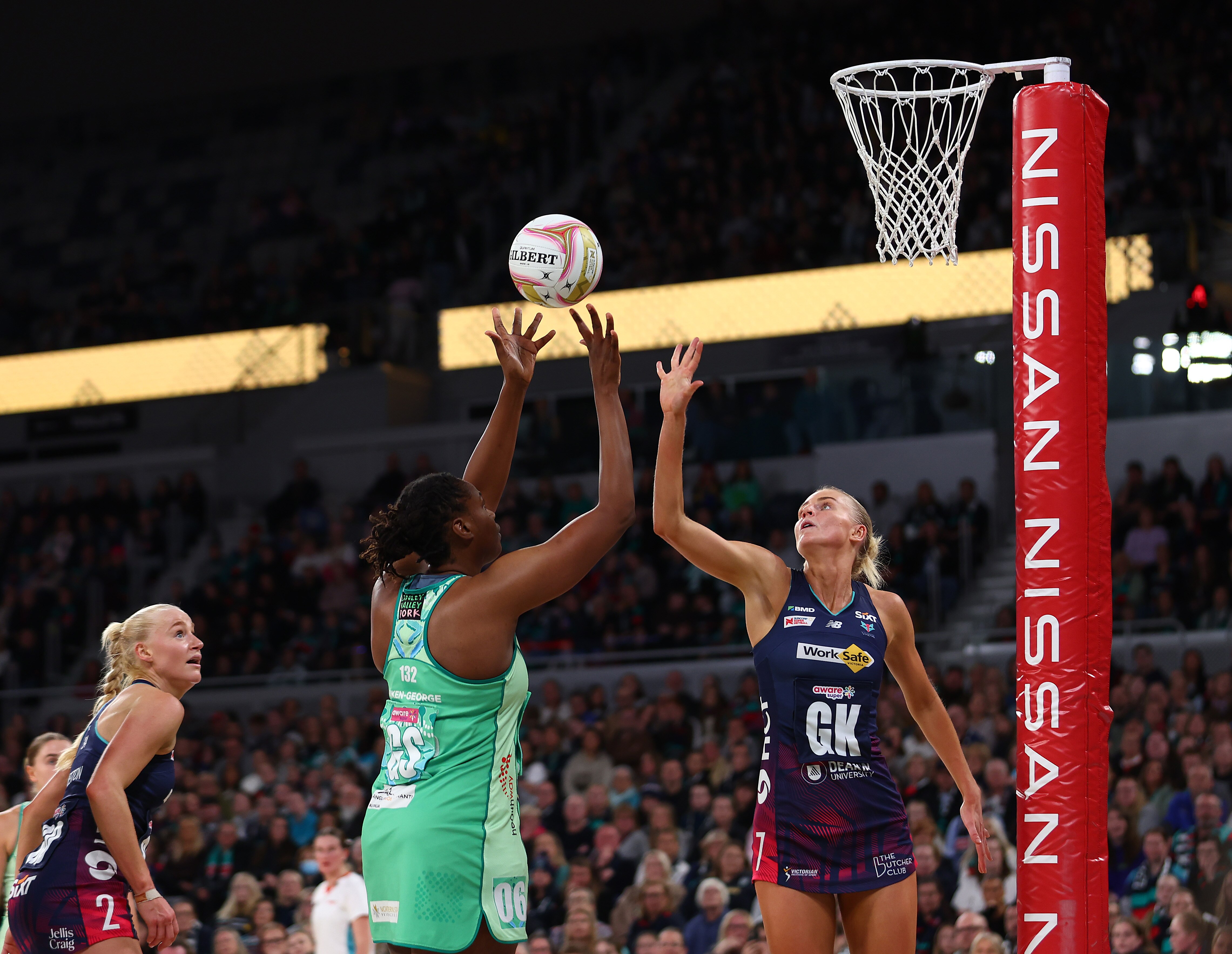 A player releases the ball aiming for goal as the opposition defends with one hand