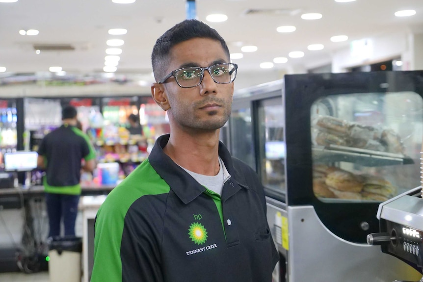 A man with glasses looks straight ahead while standing inside a service station.