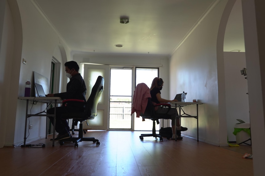 Two people silhouetted sit at their desks with light streaming in through a doorway. 