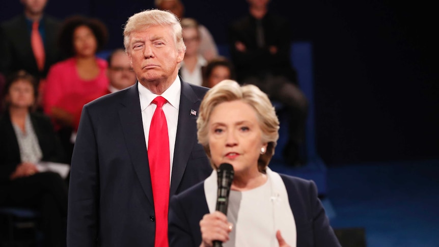 Donald Trump giving Hillary Clinton a sour look as she speaks into a microphone during a debate.