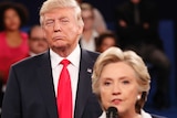 Donald Trump giving Hillary Clinton a sour look as she speaks into a microphone during a debate.