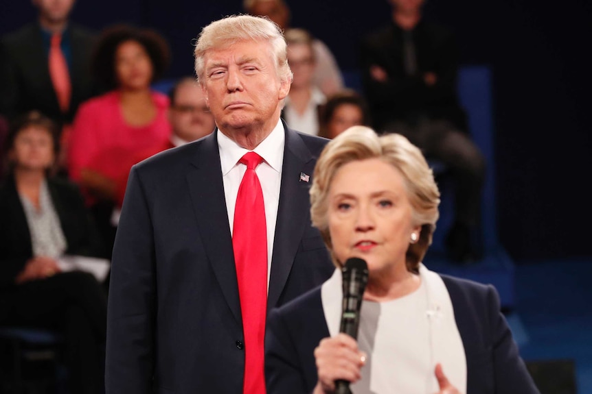 Donald Trump giving Hillary Clinton a sour look as she speaks into a microphone during a debate.